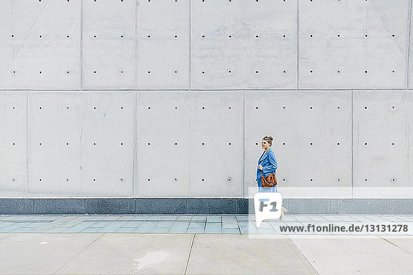 Junge Frau mit Geldbörse in Trenchcoat  die in der Stadt gegen eine Mauer läuft