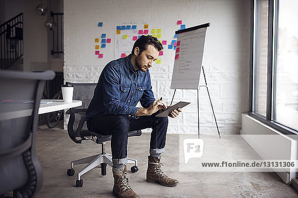 Serious businessman using tablet while sitting on chair in creative office