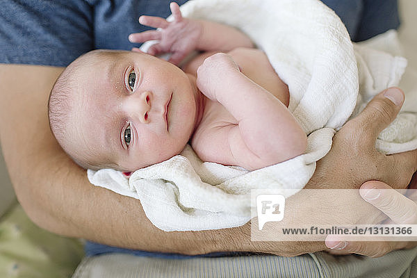 Portrait of cute newborn son carried by father at home