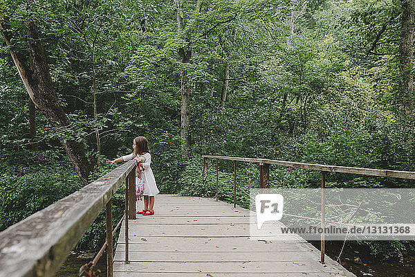 Sorgloses Mädchen in voller Länge auf Holzsteg im Wald stehend