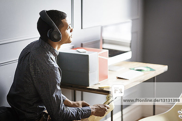Businessman looking away while listening music in office