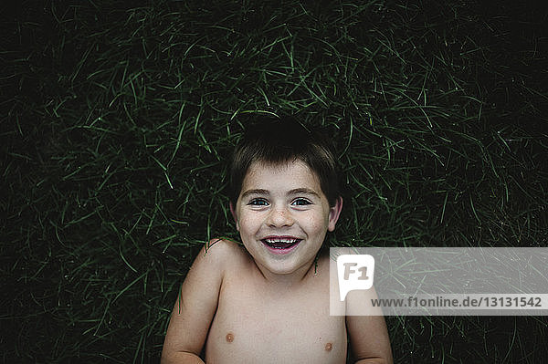 Portrait eines fröhlichen Jungen  der auf einem Grasfeld im Hinterhof liegt