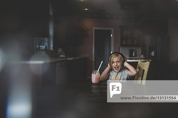 Cheerful girl listening music through tablet computer while having milkshake at table