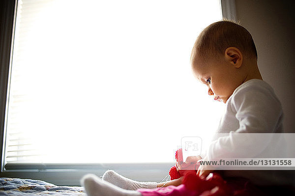 Kleines Mädchen spielt mit Spielzeug  während es zu Hause am Fenster sitzt