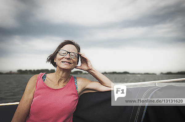 Lächelnde reife Frau sitzt auf Boot vor bewölktem Himmel