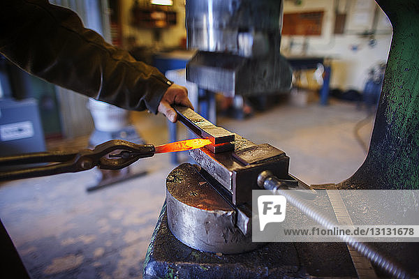 Beschnittenes Bild eines Handwerkers  der in der Fabrik heißes Metall entfernt