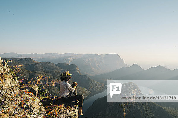 Side view of woman looking at view while sitting on mountain against clear sky