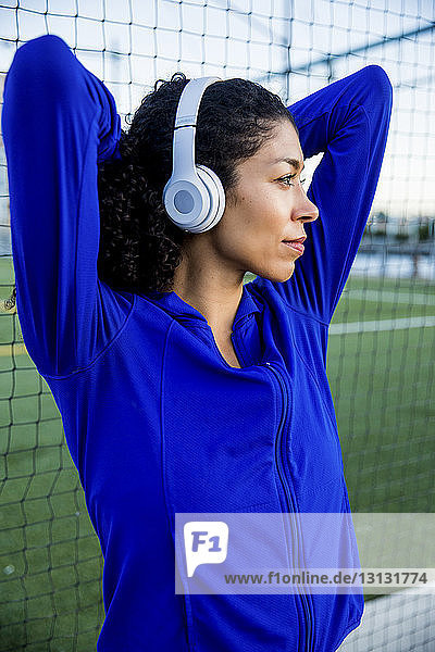 Nachdenkliche Sportlerin mit erhobenen Armen  die Musik hört  während sie am Netz steht