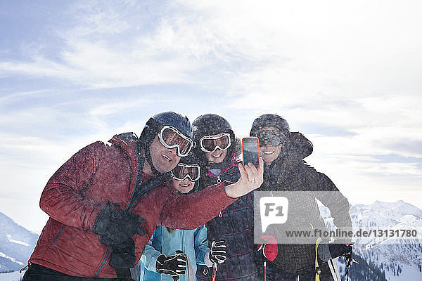 Family taking selfie with smart phone while standing at ski mountain