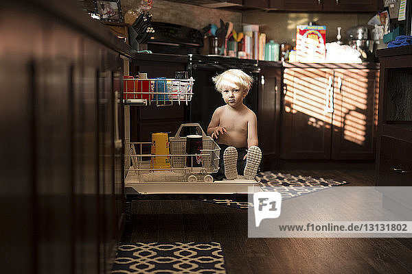 Portrait of boy sitting on drawer in kitchen