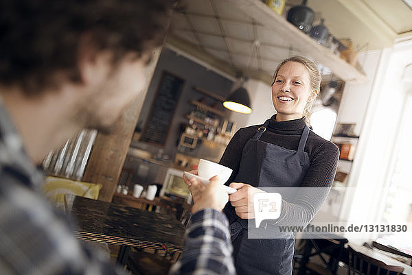Happy waitress serving coffee to man in cafe
