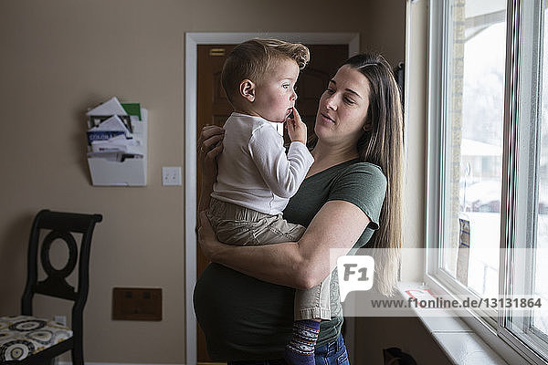 Schwangere Mutter trägt Sohn gegen Fenster zu Hause