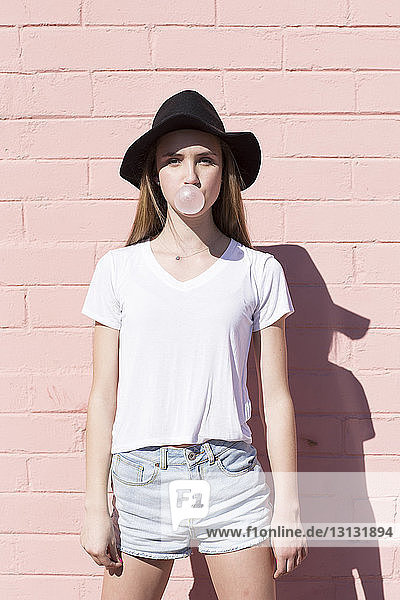 Porträt einer Teenagerin  die Kaugummi bläst  während sie an der Wand steht