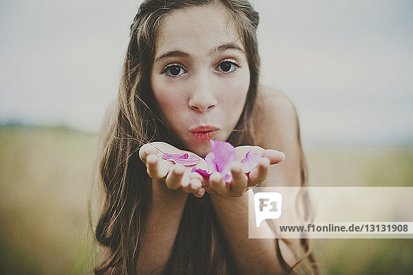 Porträt eines glücklichen Mädchens  das rosa Blütenblätter auf dem Feld bläst