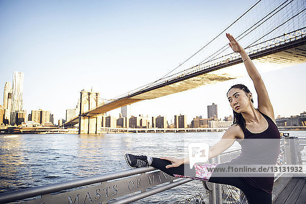 Athletin streckt Bein und Arm auf der Promenade mit der Brooklyn Bridge im Hintergrund