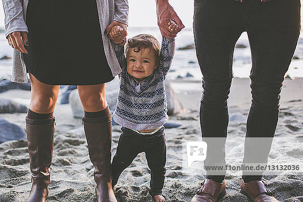 Niedriger Anteil von Eltern  die die Hände des Sohnes halten  während sie am Strand im Sand stehen