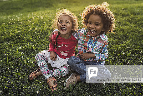 Fröhliche Geschwister sitzen auf einem Grasfeld im Park