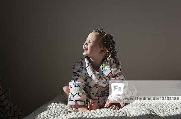 Smiling girl with eyes closed sunbathing while sitting on bed at home