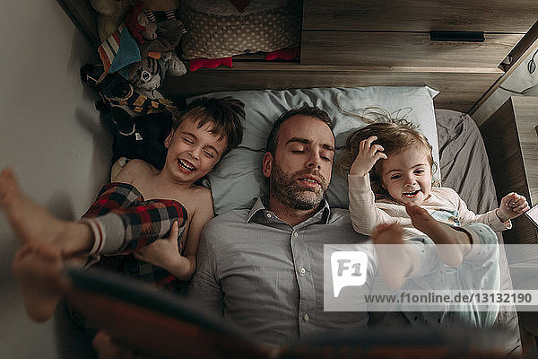 Hochwinkelansicht eines Vaterlesebuchs für Kinder  während sie zu Hause auf dem Bett liegen