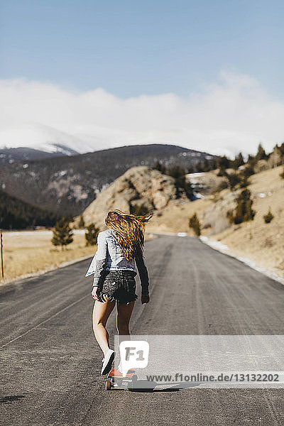 Rear view of carefree young woman skateboarding on road during sunny day