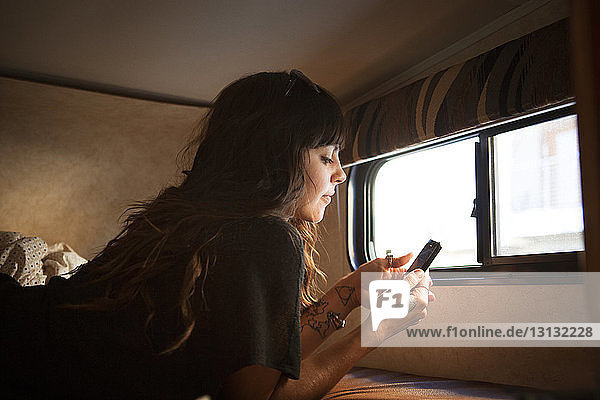 Frau benutzt Smartphone  während sie sich im Wohnmobil im Bett entspannt