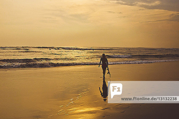 Silhouettenfrau mit Surfbrett am Strand spazieren