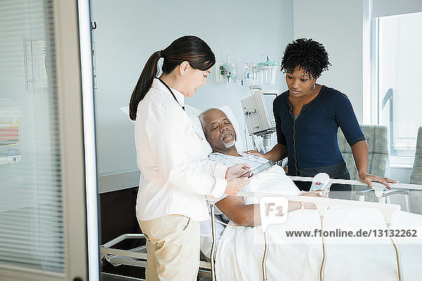 Ärztin zeigt einem älteren Patienten und einer Frau auf der Krankenhausstation einen Tablet-PC