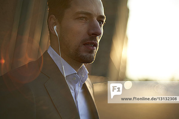 Confident businessman listening music while standing outdoors