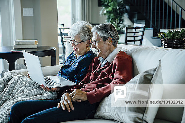 Älteres Ehepaar bei Videokonferenzen über Laptop-Computer  während es auf dem Sofa sitzt