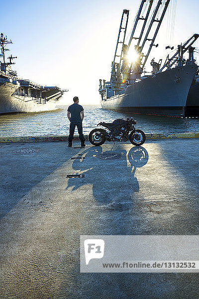 Rear view of man standing with motorcycle on road at commercial dock