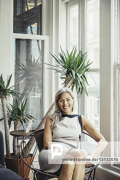 Porträt einer glücklichen Geschäftsfrau  die auf einem Stuhl in einem kreativen Büro sitzt