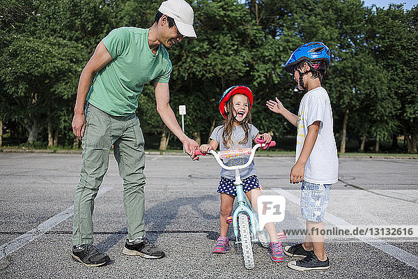Fröhliches Mädchen lernt Radfahren mit Vater und Bruder auf dem Spielplatz