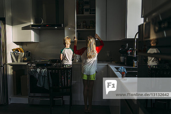 Rückansicht von Geschwistern  die zu Hause in der Küche stehen