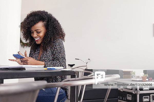 Smiling businesswoman using phone while sitting at table in office