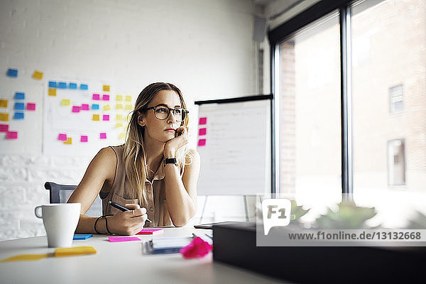 Thoughtful businesswoman sitting at table in creative office
