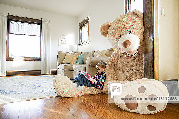 Seitenansicht eines Jungen  der zu Hause auf einem großen Teddybären sitzt und ein Spiel spielt