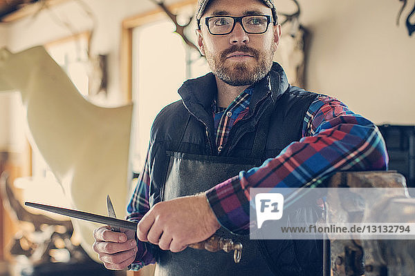 Thoughtful taxidermist holding knife and standing at workshop