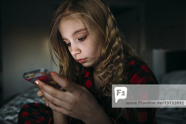 Nahaufnahme eines Mädchens  das ein Mobiltelefon benutzt  während es zu Hause auf dem Bett sitzt