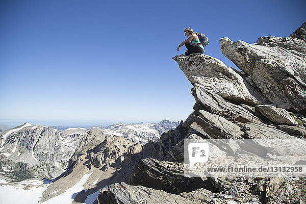 Woman with backpack sitting on rock formations against clear blue sky at Grand Teton National Park