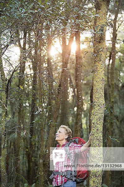 Ältere Frau mit Rucksack  die im Wald an Bäumen steht