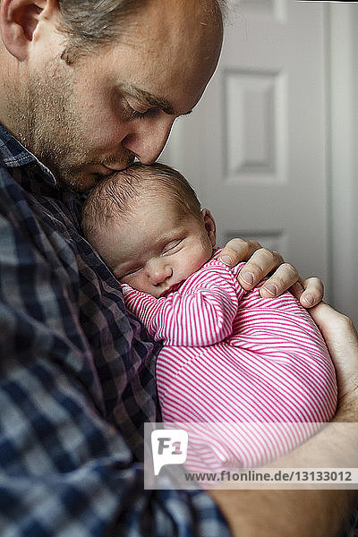 Vater küsst neugeborene Tochter  während er zu Hause sitzt