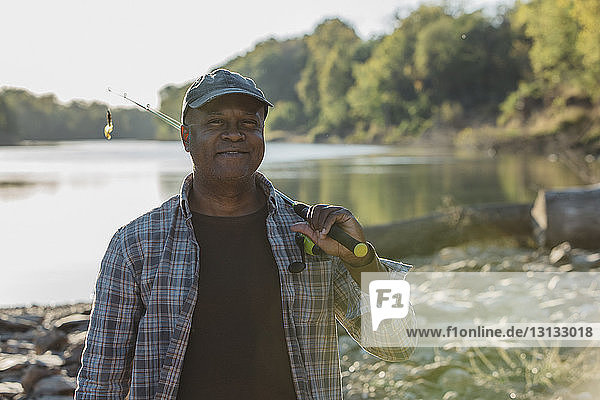 Porträt eines lächelnden Mannes mit Angelrute am Seeufer stehend