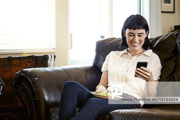 Smiling woman using phone while sitting on sofa at home