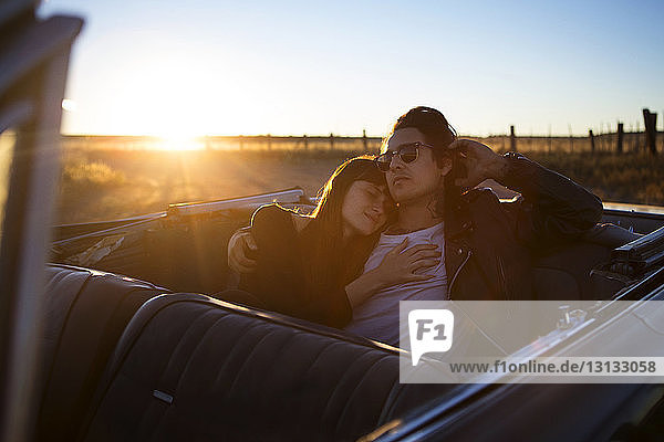 Paar entspannt sich bei Sonnenuntergang auf dem Rücksitz im Cabrio