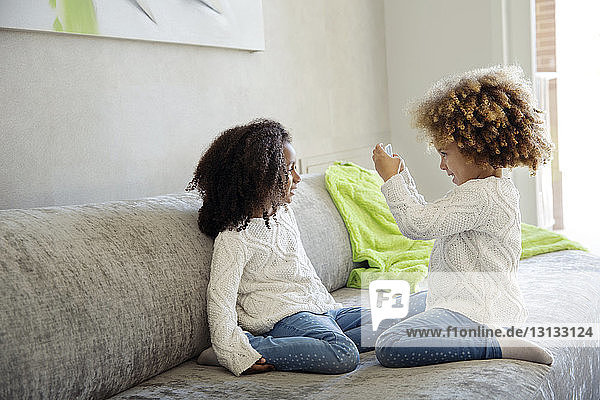 Mädchen fotografiert Schwester mit Smartphone auf Sofa