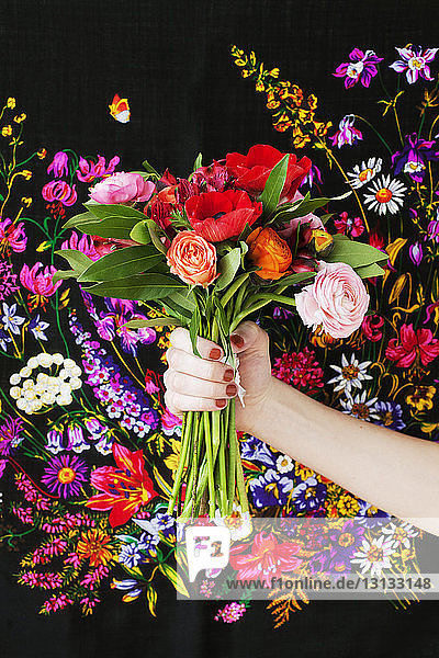 Ausgeschnittenes Bild einer Frau  die einen Rosenstrauss gegen einen Stoff mit Design hält