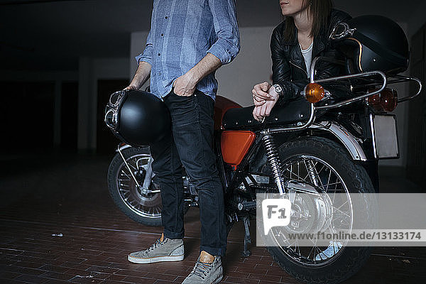 Unterer Teil eines jungen Paares  das in einer Autowerkstatt bei einem Motorrad steht