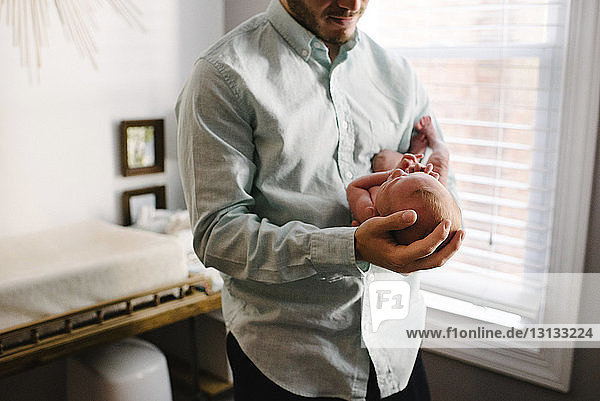 Mittelsektion eines Vaters  der eine neugeborene Tochter trägt  während er zu Hause steht