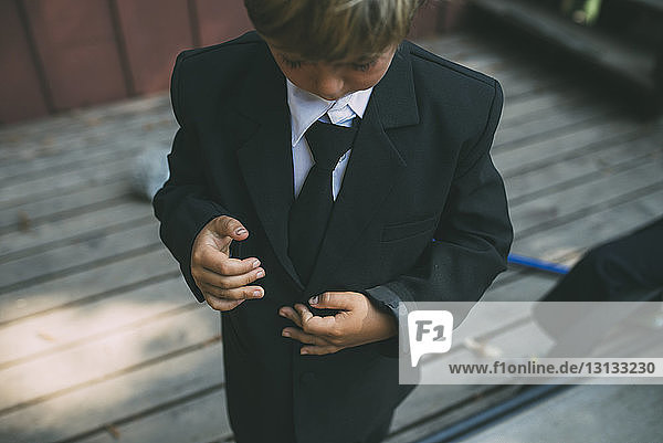 Hochwinkelansicht eines Jungen  der einen Anzug anpasst  während er auf dem Boden steht