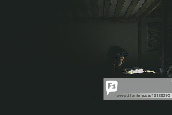 Boy using headlamp while reading book in darkroom